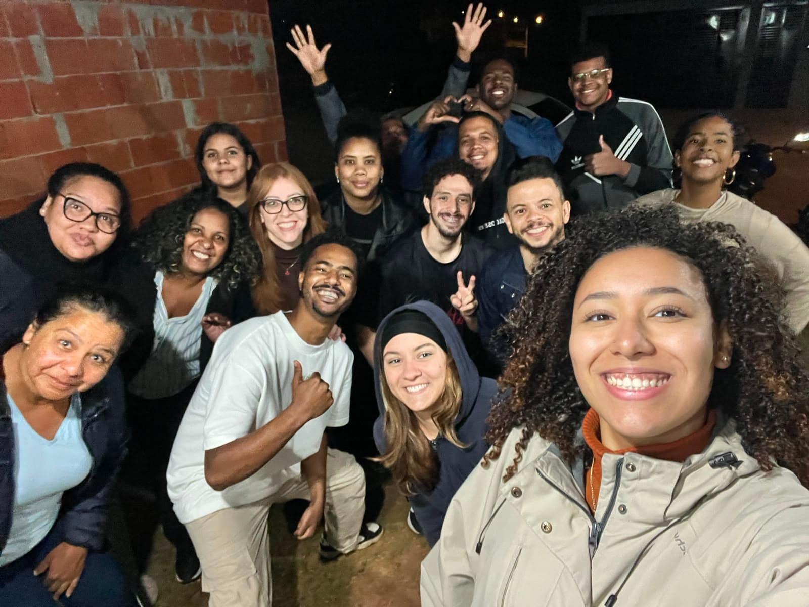 Turma de uma célula na área externa de uma casa à noite, alguns com os braços levantados, todos rindo