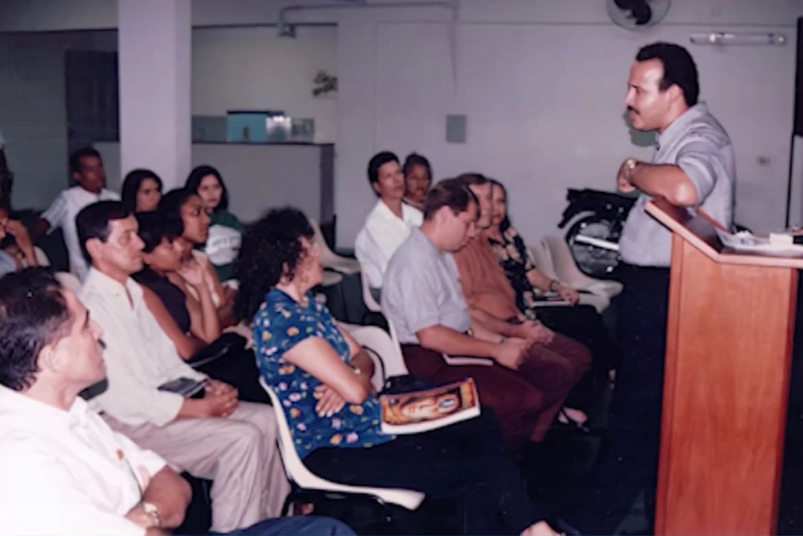 Reunião nos primeiros anos da Videira: cerca de vinte pessoas sentadas em cadeiras numa sala simples, ouvindo a pregação