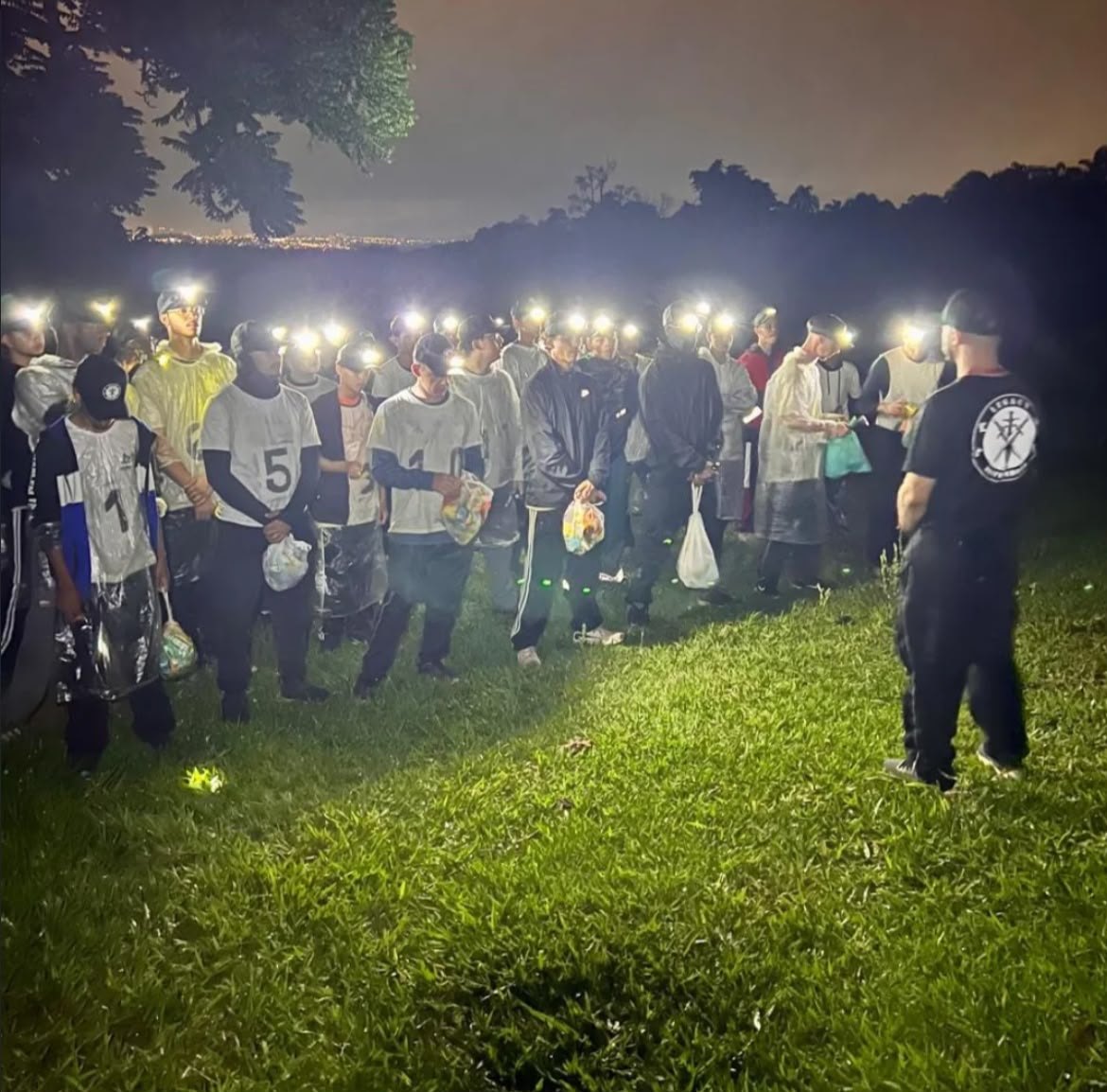 Fila de jovens de lanterna na cabeça atravessando um gramado escuro à noite