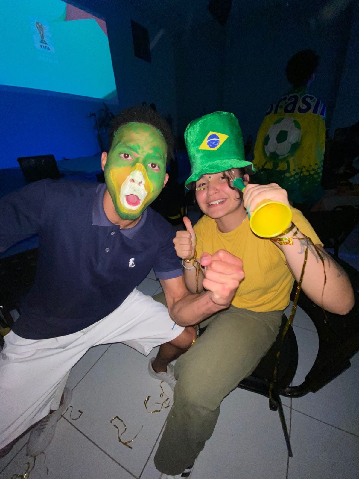 Dois rapazes com o rosto pintado de verde e amarelo posando num salão de parede azul