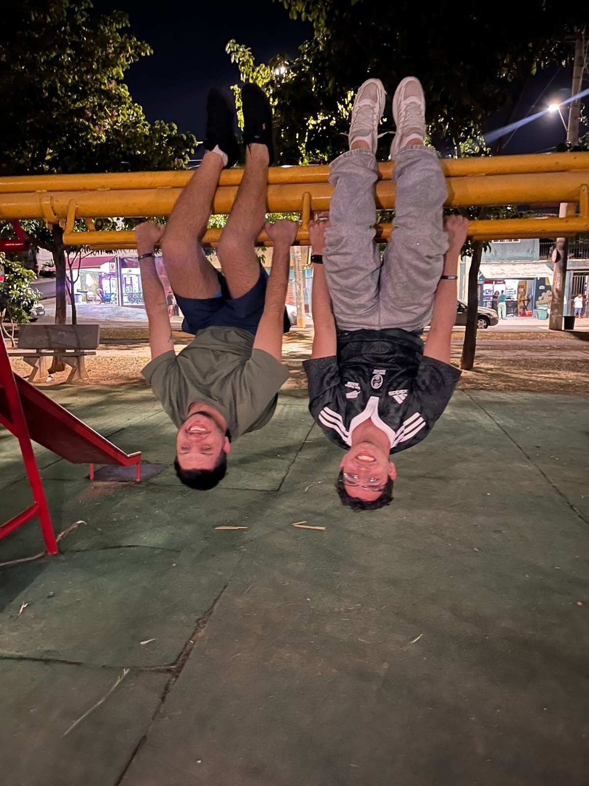Dois rapazes pendurados de cabeça para baixo na barra de um parquinho, à noite